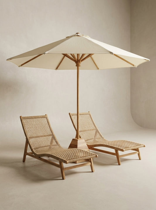Two wicker lounge chairs with a large beige umbrella on a neutral background